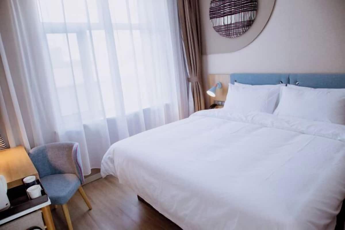 Una habitación de hotel con una cama grande, una silla, una mesita de noche y una lámpara.