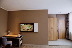 A hotel room with a desk, chair, and a television mounted on the wall.
