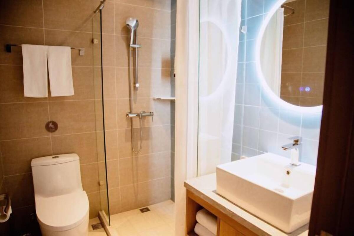 Un baño moderno con ducha envuelta en vidrio, un lavamanos blanco y un inodoro.