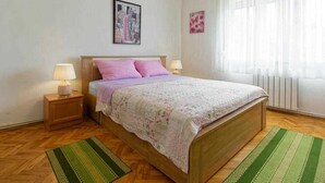 A bedroom with a wooden bed, two bedside lamps, a green and white striped rug, a cityscape picture on the wall, and a window with sheer curtains. - Apartment Sunce 2 close to the beach (Umag)