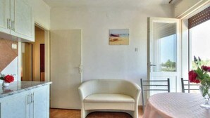 A room with a curved sofa, a dining table with a vase of flowers, a cabinet with a vase of flowers, and a painting on the wall. - Apartment Sunce 2 close to the beach (Umag)