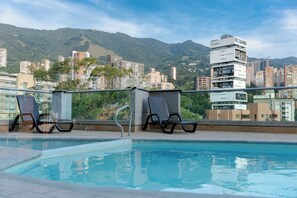 A swimming pool with two lounge chairs and a view of a cityscape with mountains in the background. - Stylish Apt el poblado by Hoost APT 608 (Medellín)