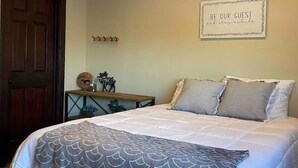 A bedroom with a bed, a wall-mounted sign, a coat rack, and a small table with decorative items.