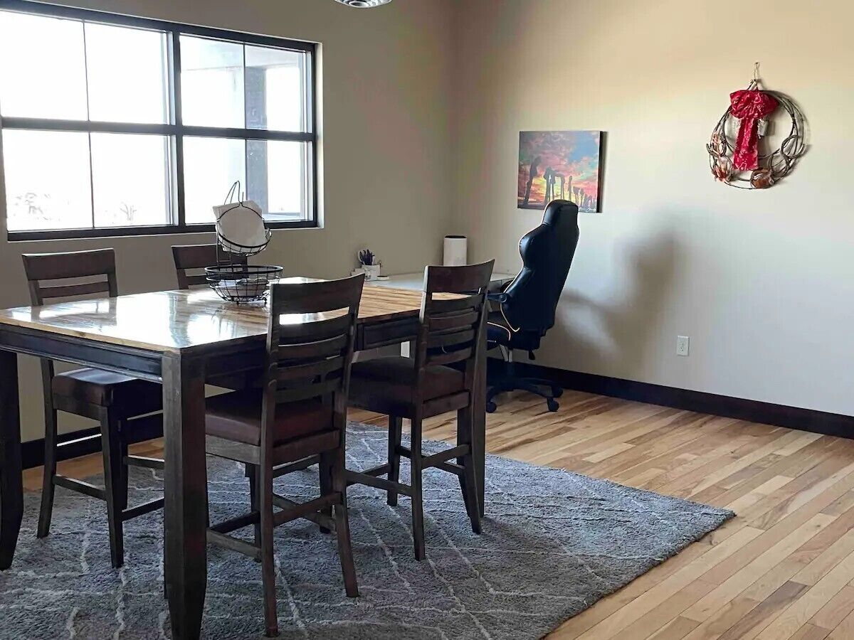 A dining area with a wooden table and chairs, a rug, and a painting on the wall.