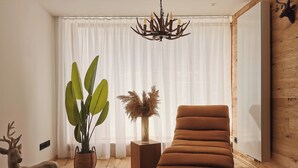 A modern living room with a wooden floor, a brown sofa, a large green plant, a decorative deer statue, and a chandelier. - Alpenperle im Zentrum von Erfurt/nähe Domplatz (Erfurt)