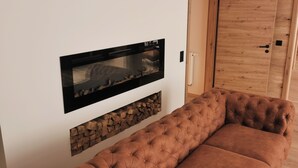 A modern living room with a large flat-screen TV mounted on the wall, a tufted brown sofa, a wooden cabinet, and a fireplace with a log display. - Alpenperle im Zentrum von Erfurt/nähe Domplatz (Erfurt)