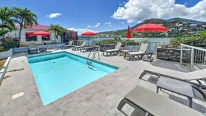 Un espace piscine aménagé sur le toit, avec des chaises longues et des parasols, offrant une vue panoramique sur le paysage côtier.