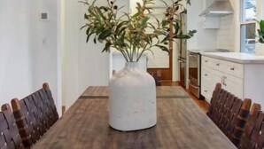 Een eetgedeelte met een houten tafel, een witte vaas als middelpunt en een hangende kroonluchter.
