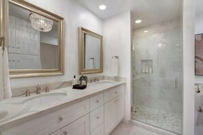 Un baño moderno con dos lavamanos, un espejo grande y una ducha con cerramiento de vidrio.