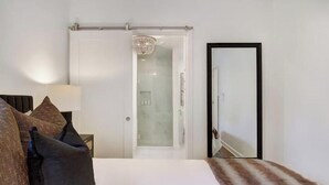 Een hotelkamer met een bed, nachtkastje, lamp, spiegel en een deur naar een badkamer.