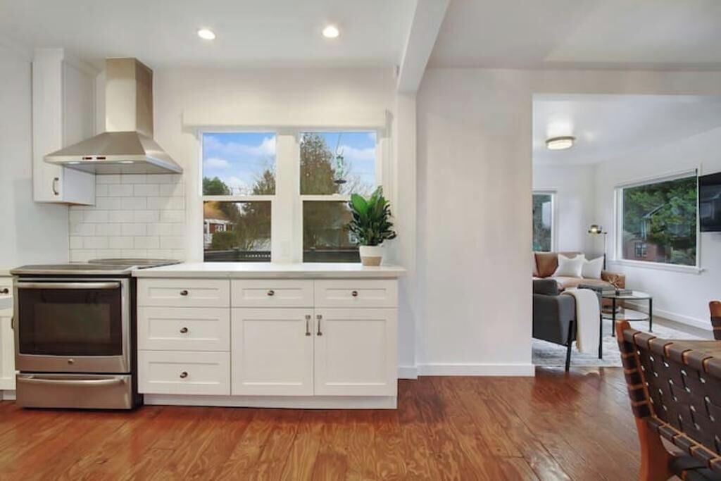 A modern kitchen with white cabinetry, a built-in oven, and a window overlooking a garden.