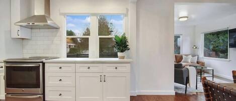 A modern kitchen with white cabinetry, a built-in oven, and a window overlooking a garden.