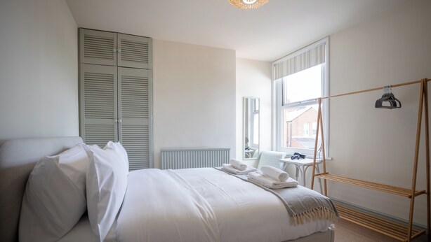 Een slaapkamer met een bed, een kledingkast, een raam en een droogrek.