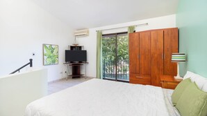 Een slaapkamer met een groot bed, een houten kledingkast, een televisie op een standaard, en een raam met uitzicht op groen.
