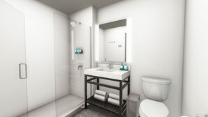 Un baño moderno con cabina de ducha de vidrio, un lavabo blanco con marco oscuro y un inodoro.
