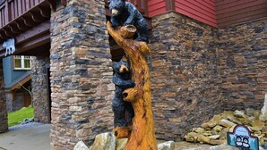 A wooden sculpture of bears on a tree trunk in front of a stone building with a red roof.