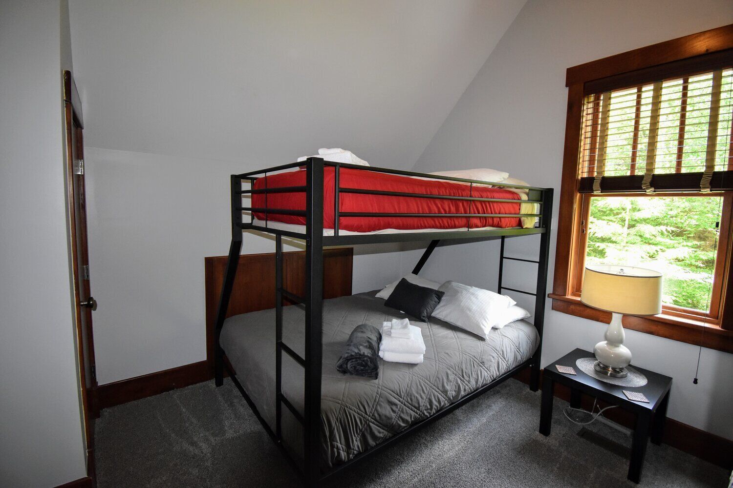 Un lit superposé avec une literie rouge, un matelas gris et une table de chevet avec une lampe.