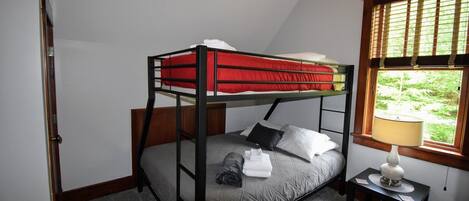 Un lit superposé avec une literie rouge, un matelas gris et une table de chevet avec une lampe.