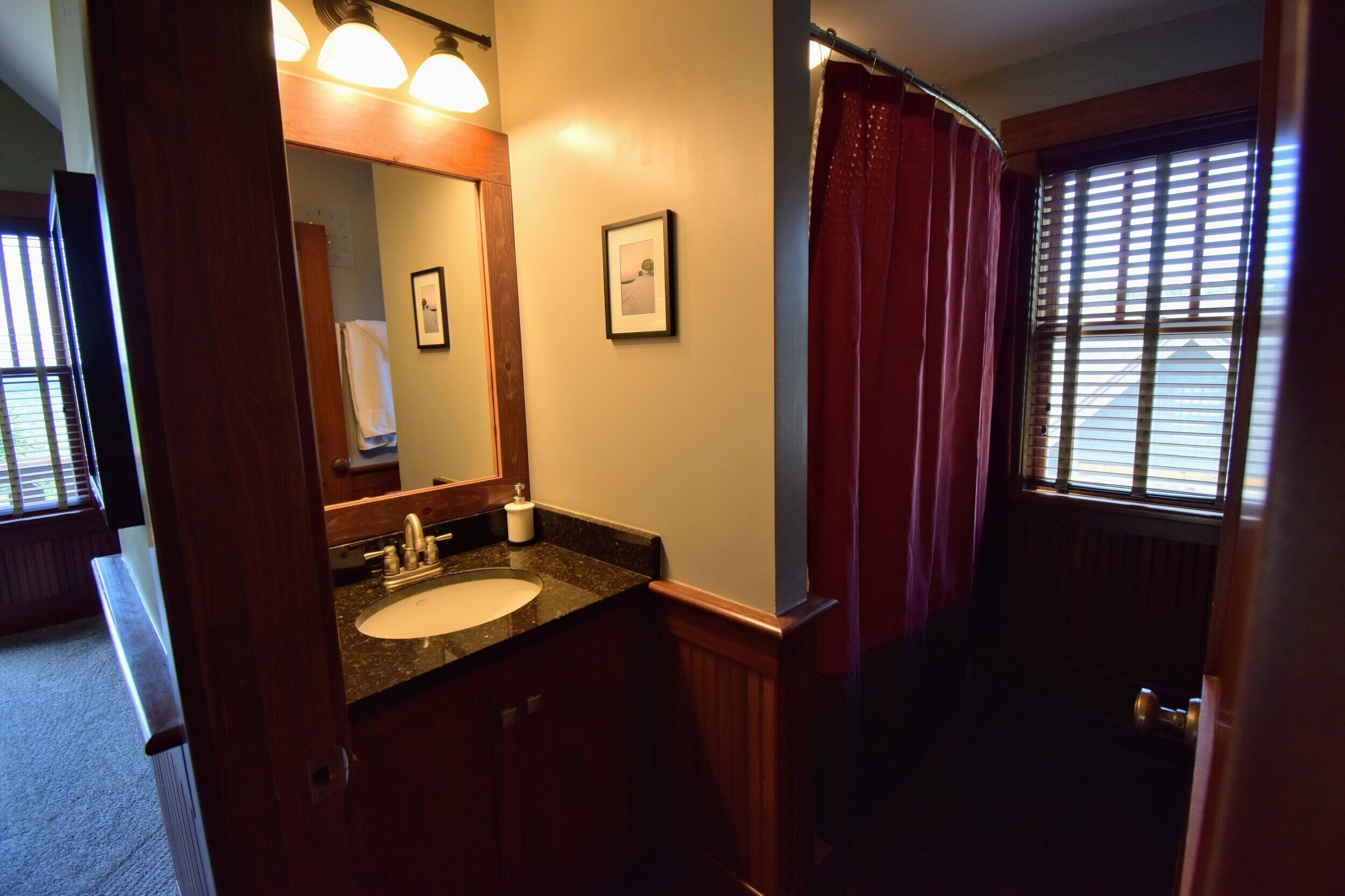 Une salle de bain avec un lavabo, un miroir et une fenêtre équipée de stores.