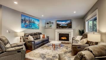 A living room with a fireplace, leather sofas, a flat-screen TV, and artwork on the walls.