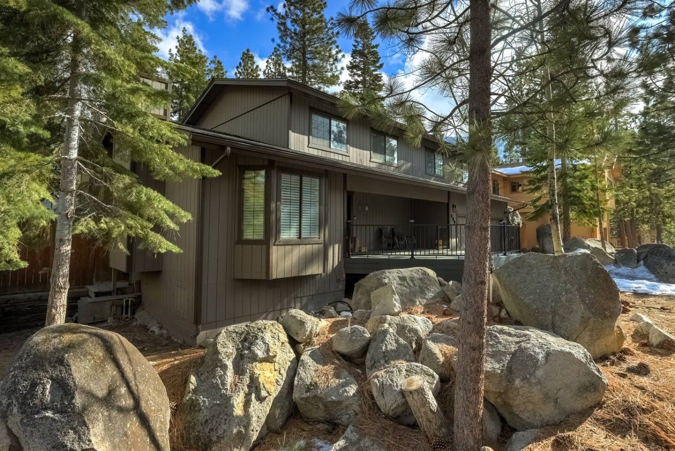 A two-story cabin with a covered porch and large rocks in the foreground.