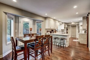 A modern kitchen with a central island, wooden chairs, and bar stools. - Modern 5BR Home | Chef’s Kitchen | BBQ | Sleeps 10 (Stateline)