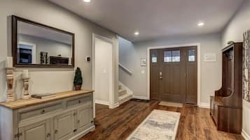 Um corredor com piso de madeira, um console com espelho, uma porta com painéis de vidro jateado e uma placa de boas-vindas.
