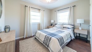 A bedroom with a large bed, two bedside tables, a ceiling fan, and two windows with curtains. - Downtown Winter Garden bungalow with private putting green and fire pit (Winter Garden)