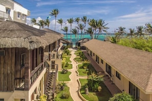 A resort with thatched-roof buildings, a central pathway, and a view of the ocean.