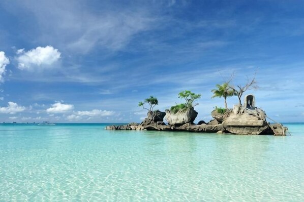 A clear turquoise sea, a rocky island with sparse vegetation, and a clear sky.