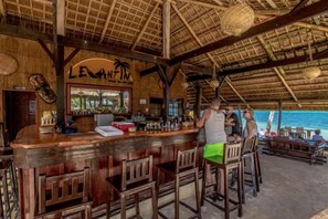 A bar area with a thatched roof, wooden bar counter, and stools. - Levantin Boracay (Boracay Island)