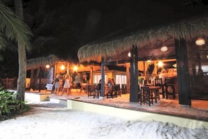 Un espacio de comedor al aire libre con estructuras de techo de paja, mesas y sillas.