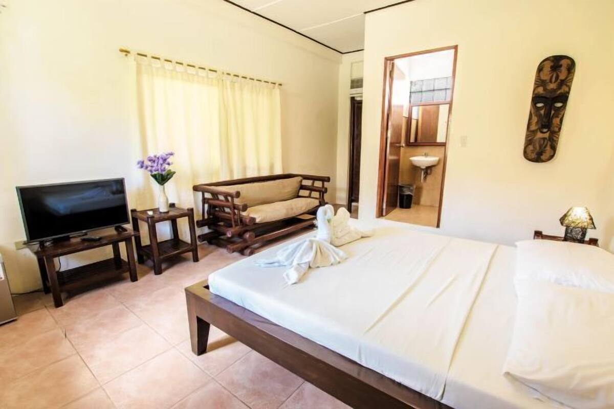 Une chambre d’hôtel équipée d’un lit, d’une télévision, d’un canapé, d’un miroir et d’une œuvre d’art accrochée au mur.