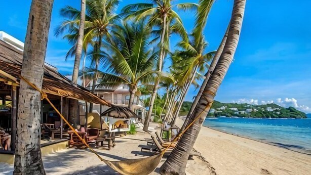 A beach with palm trees, a hammock, and a building with outdoor seating. - Levantin Boracay (Boracay Island)