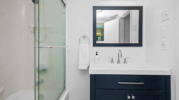 Un baño moderno con ducha de vidrio, un lavabo blanco con gabinete oscuro y un espejo sobre el lavabo.