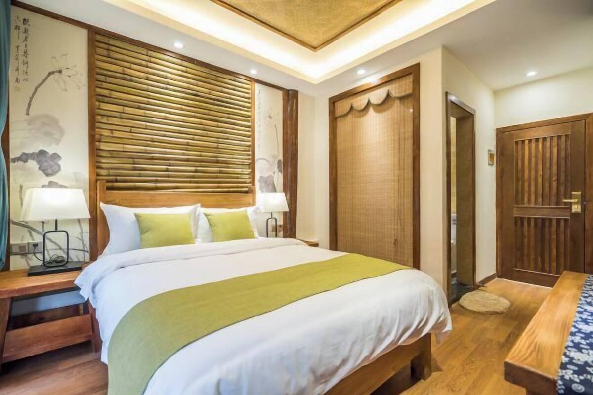 Una habitación de hotel ordenada con una cama grande, cabecero de madera y un panel de pared de estilo tradicional japonés.