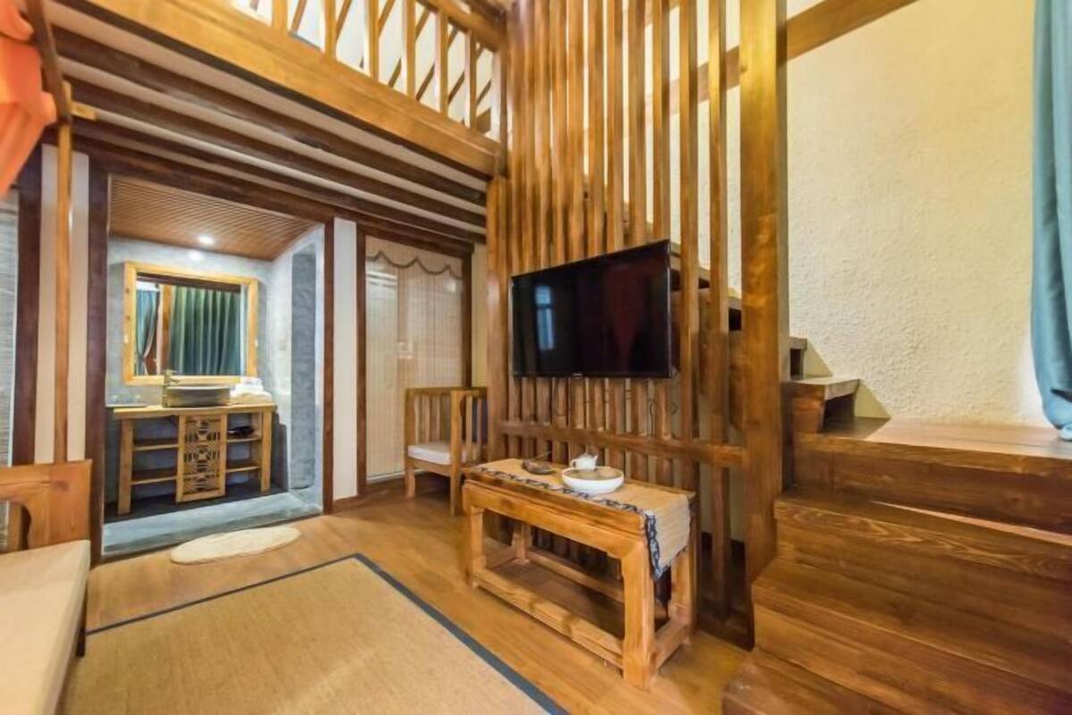 Una habitación tradicional japonesa con suelo de tatami, una mesa de madera baja con un juego de té, un televisor montado en una pared de madera y una puerta corredera que da a otra habitación.