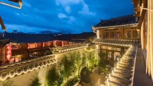 A traditional courtyard with tiled roofs and wooden structures, surrounded by lush greenery. - Yuetu Shishanju, Lijiang Ancient City (Lijiang)