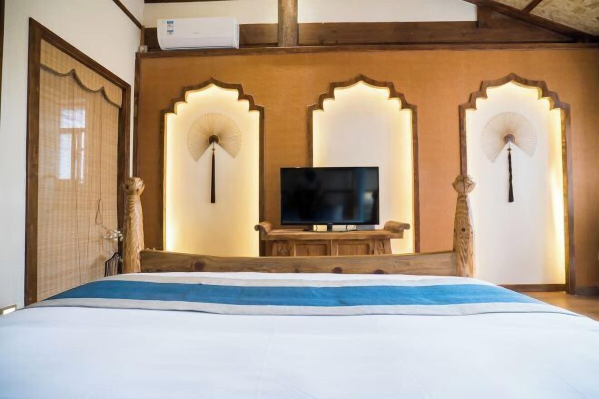 A hotel room with a bed, a television on a wooden stand, and decorative wall fans.
