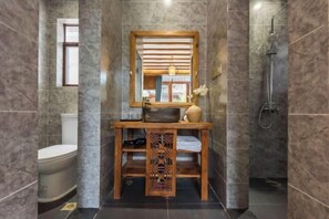 A bathroom with a marble wall, a wooden vanity with a mirror, a toilet, and a shower area. - Yuetu Shishanju, Lijiang Ancient City (Lijiang)