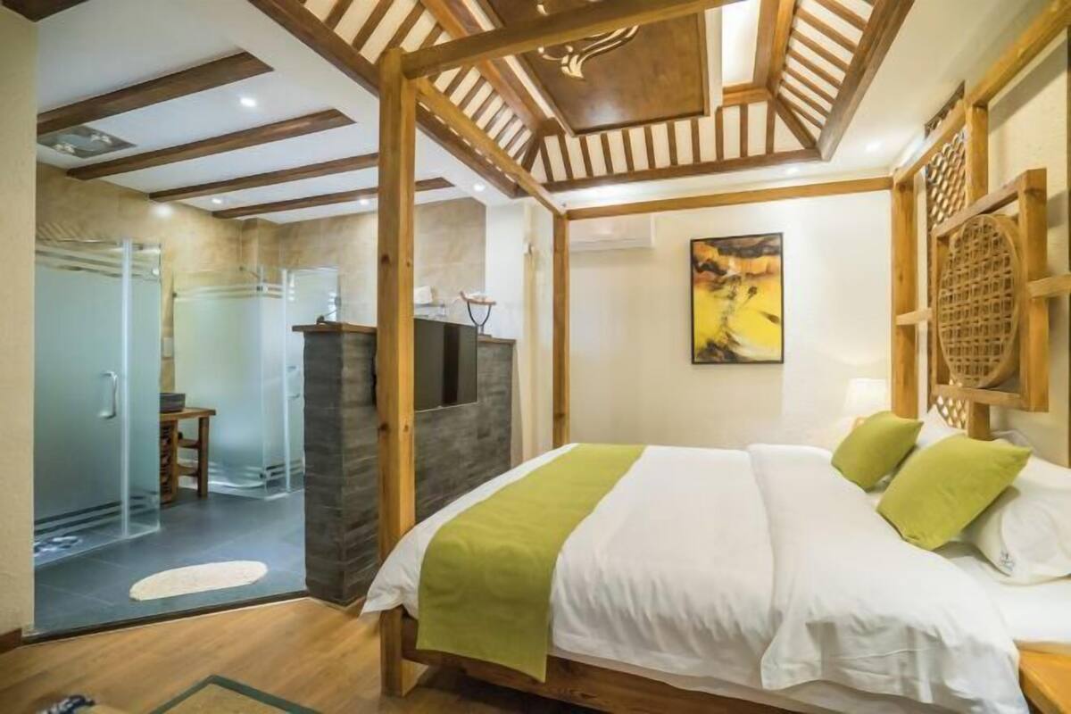 Un dormitorio con cama, vigas de madera, ducha de vidrio y un cuadro en la pared.