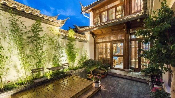 A traditional courtyard with a wooden deck, potted plants, and a building with tiled roof and wooden lattice windows. - Yuetu Shishanju, Lijiang Ancient City (Lijiang)