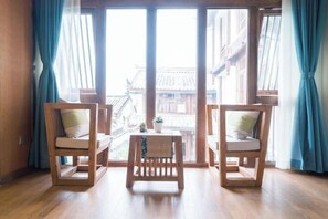 A room with two wooden chairs and a small table, large windows with curtains, and a view of traditional buildings. - Yuetu Shishanju, Lijiang Ancient City (Lijiang)