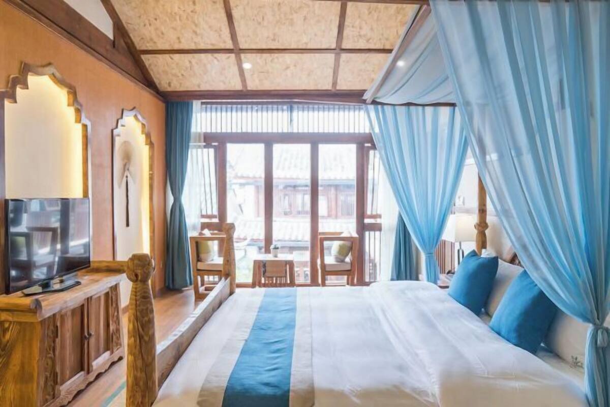 Un dormitorio con una cama grande, un televisor sobre un mueble de madera y vistas al exterior a través de amplias ventanas.