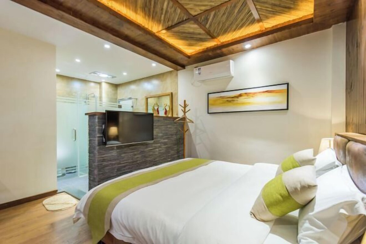 A hotel room with a bed, a TV, a stone wall, and a painting on the wall.