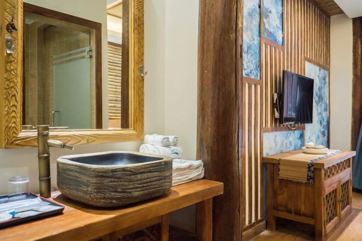 A bathroom with a stone basin, wooden vanity, a mirror, towels, and a television.