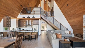 A spacious loft with a high ceiling, a mezzanine level, a kitchen with modern appliances, a dining area, and a living room with a sofa and coffee table.