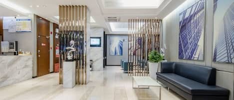 A hotel lobby with a reception desk, seating area, and a large window with a view.