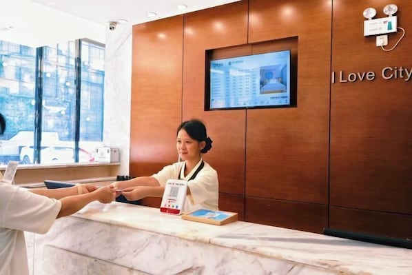 A hotel reception desk with a digital screen displaying information, a receptionist, and a marble counter.