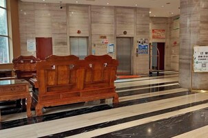 Un vestíbulo de hotel con un banco de madera, suelo de mármol, ascensores y un mostrador de recepción.